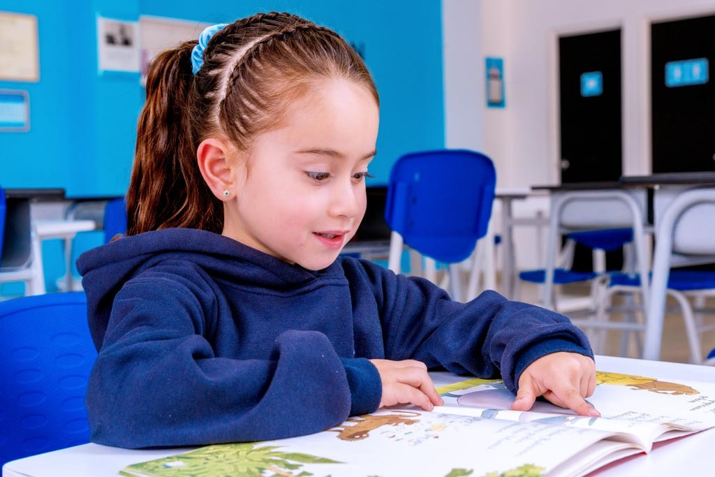 Niña leyendo en un centro Kumon, con postura adecuada, desarrollando habilidades de comprensión y síntesis.